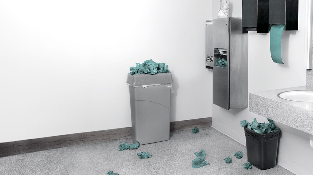 Washroom with paper towels on the floor and in overflowing bins